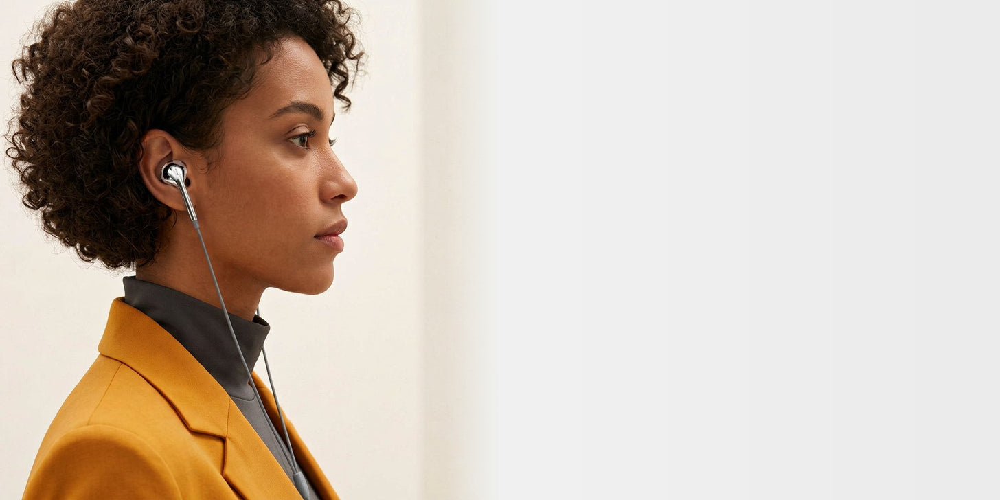 Adult model wearing silver LUMEAR wired earbuds in a saffron studio editorial